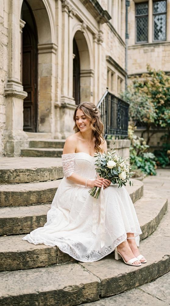 A bride in an off-shoulder ivory midi wedding dress on stone courthouse steps, soft afternoon light