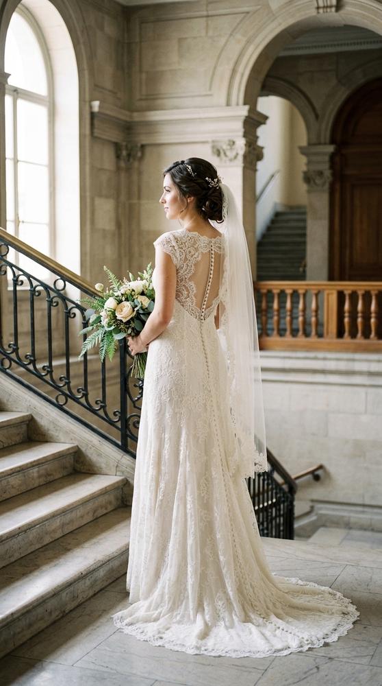 A bride in an ivory vintage-style lace wedding dress with covered buttons down the back in a historic courthouse