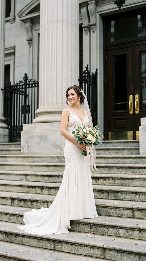 A bride in an ivory fit-and-flare wedding dress with a V-neckline on courthouse steps, soft daylight